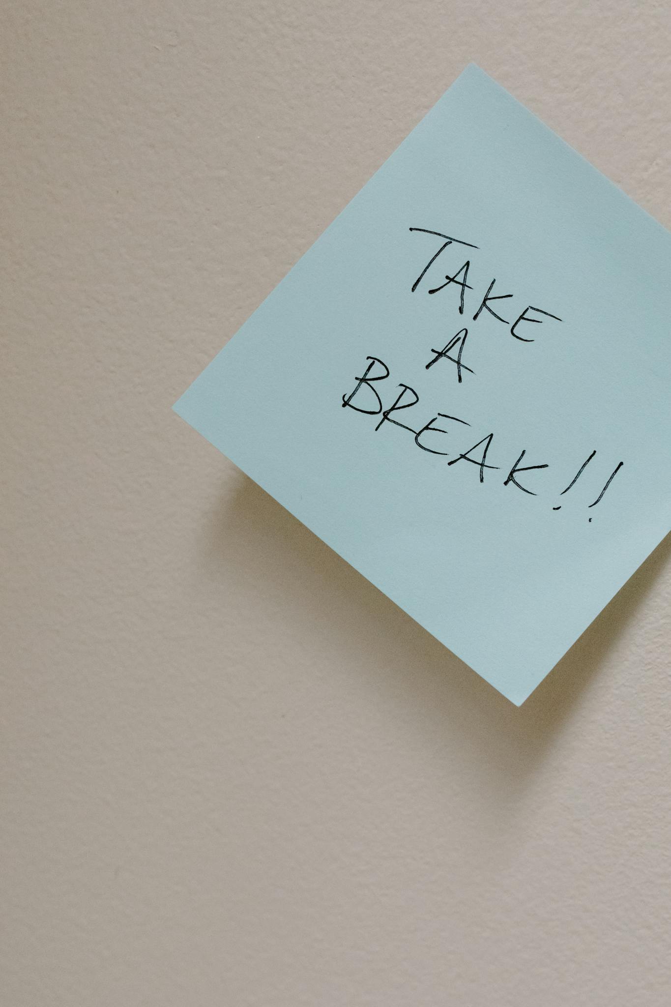 Close-up of a sticky note with 'Take a Break!!' message on a plain wall.